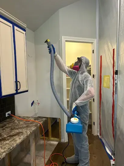 Technician in a protective suit applying antimicrobial in a kitchen during water damage cleanup in Monroe Township