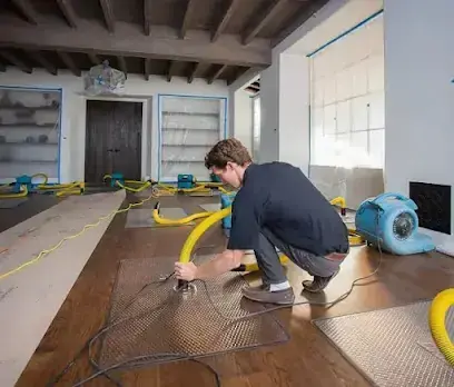Technician setting floor drying mats on a wet hardwood floor in Monroe Township