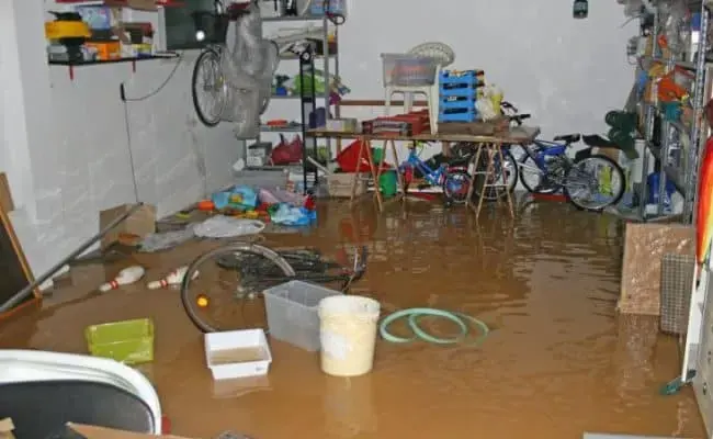 Brown flood water covering the floor of a basement storage area with bikes and shelving in a Monroe Township home