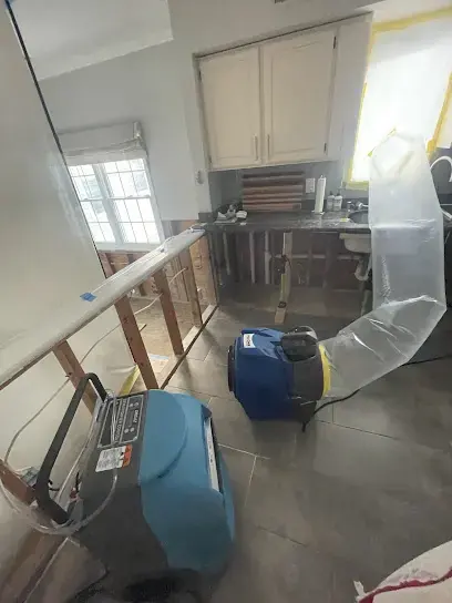 Dehumidifier and air mover running behind plastic containment in a Jamesburg room during drying