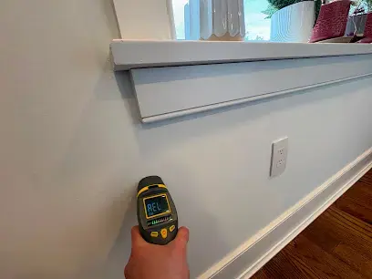 A hand holding a moisture meter against a painted wall inside a Freehold, NJ home