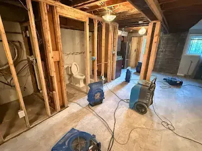 Air movers and a dehumidifier drying opened wall framing in a Monroe Township basement